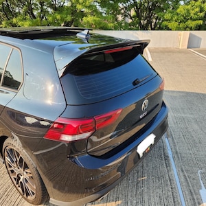 May include: A black Volkswagen GTI hatchback car with a sunroof, spoiler, and tinted windows. The car has red accents and GTI badging. The image is taken outdoors in daylight.