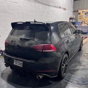 May include: A black Volkswagen Golf with a rear spoiler and a number plate that reads "FTD1340". The car is parked in a garage and has a blue cord on the ground next to it.