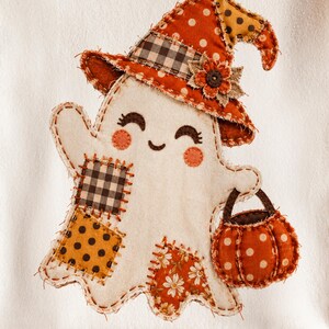 May include: A cream-colored fabric ghost applique featuring a witch hat with orange polka dots and black plaid, a pumpkin bucket, and various fabric patches including floral, polka dot, and plaid patterns with visible stitching on a white background.
