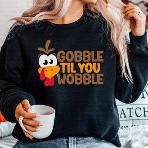 May include: Black sweatshirt with a cartoon turkey face and the text "Gobble Til You Wobble" in orange and brown letters.
