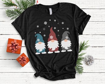 May include: Black t-shirt with a design of three gnomes wearing hats and standing in front of a snowflake pattern.