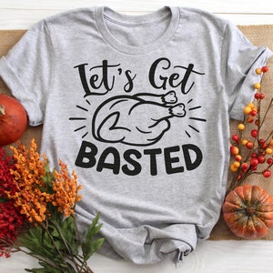 May include: A gray t-shirt with the text "Let's Get Basted" and a cartoon image of a turkey. The text is in black and the turkey is in black and white.