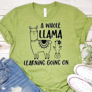 May include: A green t-shirt with a black llama wearing glasses and a cactus with a heart. The text on the shirt reads "A Whole Llama Learning Going On".