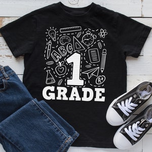 May include: Black t-shirt with a white graphic of school supplies and the number "1" with the text "GRADE" underneath.