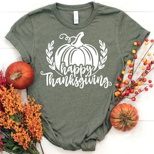Puede incluir: Una camiseta verde con una calabaza blanca y el texto "Happy Thanksgiving".
