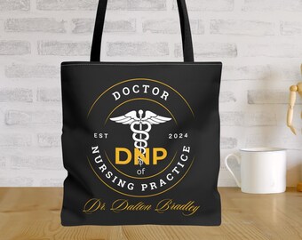 Puede incluir: Bolsa de tela negra con un círculo blanco que contiene un símbolo de caduceo médico y el texto "Doctor of Nursing Practice, DNP, Est 2024" en blanco. El texto "Dr. Dalton Bradley" está impreso en dorado debajo del círculo.