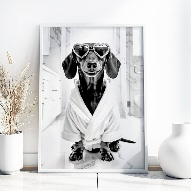 May include: A black and white photo of a dachshund wearing heart-shaped sunglasses and a white bathrobe. The dog is sitting on a white tiled floor.