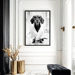May include: A black and white photograph of a dachshund wearing heart-shaped sunglasses and a white bathrobe. The dog is sitting on a white tiled floor in a bathroom.