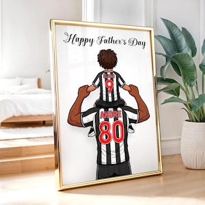 Pu&ograve; includere: Opera d'arte incorniciata con una cornice dorata. L'immagine raffigura un padre che porta un bambino sulle spalle, entrambi con maglie da calcio a strisce bianche e nere. Il testo "Happy Father's Day" &egrave; in alto.