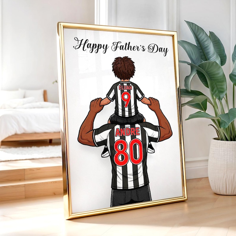 Pu&ograve; includere: Opera d'arte incorniciata con una cornice dorata. L'immagine raffigura un padre che porta un bambino sulle spalle, entrambi con maglie da calcio a strisce bianche e nere. Il testo "Happy Father's Day" &egrave; in alto.