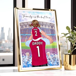 May include: A digital illustration of a father and daughter wearing matching soccer jerseys. The father is holding the daughter on his shoulders. The father's jersey says "Daddy 1" and the daughter's jersey says "Avie 2". The background is a blurred image of a soccer stadium with a crowd of people. The text "Family is the best team" is at the top of the image.