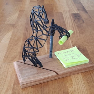 Peut inclure: Une sculpture de cheval géométrique noire avec un porte-stylo et un post-it jaune sur lequel est écrit "Ne remets pas à demain ce que tu peux faire après demain".