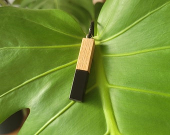 May include: A black and wood pendant necklace. The pendant is a rectangular shape with a black resin top and a wood bottom.