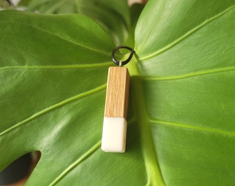 May include: A wooden and white pendant with a black metal bail. The pendant is rectangular and has a smooth, polished finish.