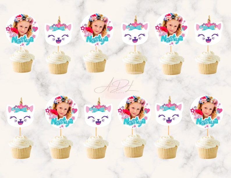May include: Twelve cupcake toppers featuring a white cat face with a unicorn horn, pink flowers, and a blue bow. Each topper also includes a circle with a girl's photo and the name "Nastya" in pink and blue lettering.