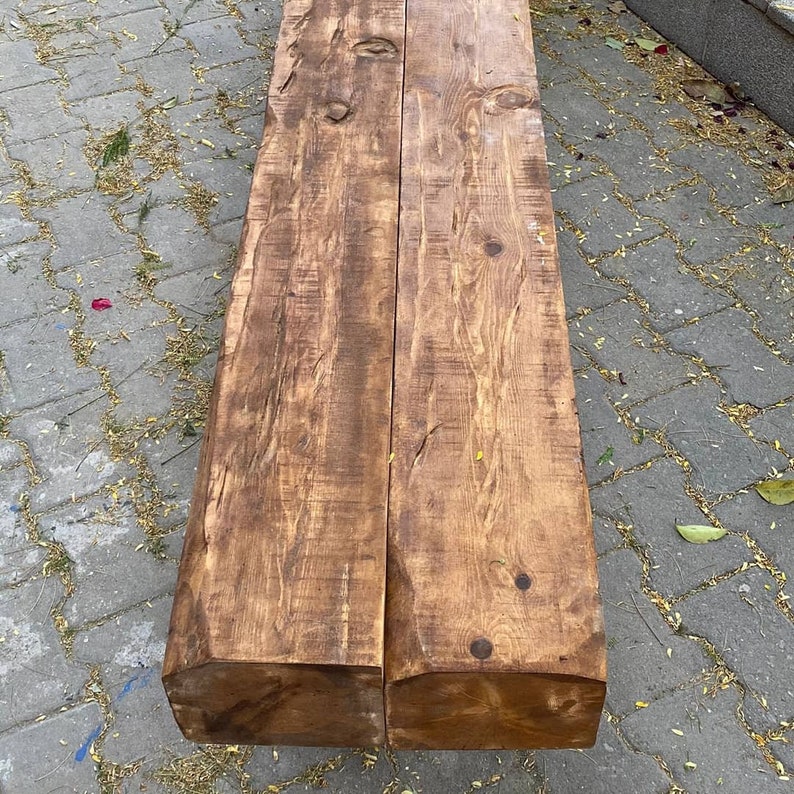 May include: A rustic wooden bench made from two thick planks of wood. The wood has a natural brown color and a rough, textured surface.