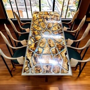May include: A long, rectangular dining table with a unique geometric design made of wood and resin. The table is surrounded by six chairs with a modern design.