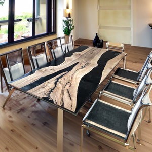 May include: A large wooden dining table with a black epoxy resin inlay. The table has a natural wood grain pattern and is supported by four metal legs. The table is surrounded by six chairs with black fabric seats and chrome frames.