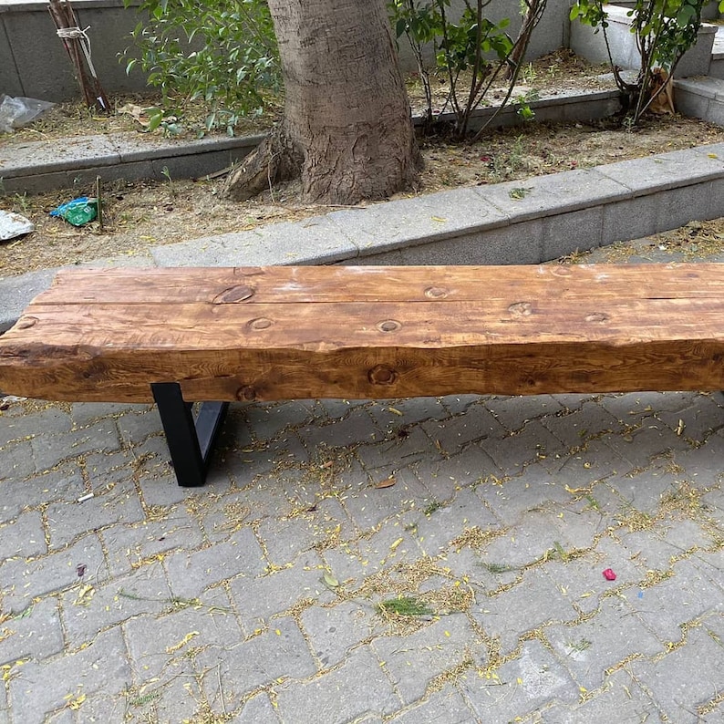 May include: A rustic wooden bench with a natural wood finish and black metal legs. The bench is made from a single piece of wood and has a rough, textured surface.