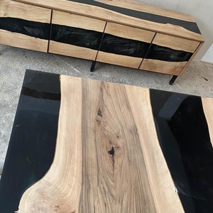 May include: A wooden coffee table with a black epoxy resin inlay. The table has a natural wood grain and a live edge design.