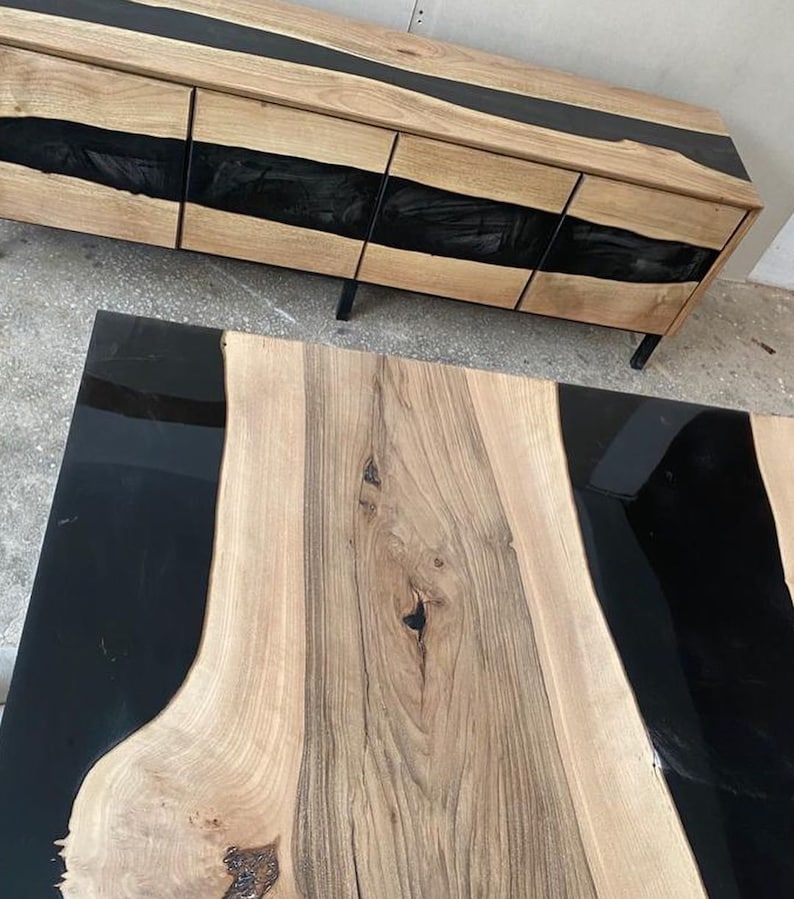 May include: A wooden coffee table with a black epoxy resin inlay. The table has a natural wood grain and a live edge design.