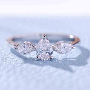 Könnte beinhalten: Ein silberner Ring mit drei birnenförmigen Diamanten. Der mittlere Diamant ist größer als die beiden Diamanten an den Seiten.