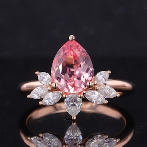 May include: A pear-shaped pink gemstone ring with a halo of smaller clear gemstones set in rose gold.