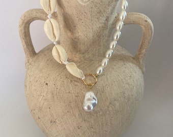 May include: A white shell and pearl necklace with a gold pendant hanging from a ceramic vase.