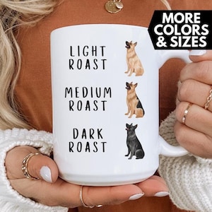 Op de afbeelding: Witte keramische mok met een illustratie van een Duitse herder en de tekst "Light Roast", "Medium Roast" en "Dark Roast".