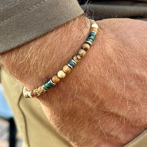 Puede incluir: Un brazalete de cuentas con cuentas marrones, verdes y blancas. El brazalete está en la muñeca de una persona.