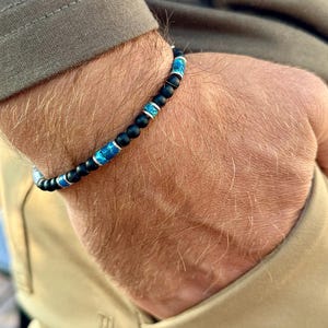 May include: A black beaded bracelet with blue and silver accents. The bracelet is worn on a person's wrist.