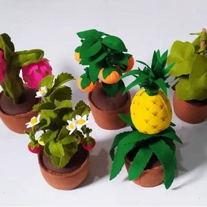May include: A selection of felt potted plants, featuring a dragon fruit, strawberry, orange tree, pineapple, and a green fruit with yellow flowers. Each plant is in a brown pot, with bright colours and detailed craftsmanship.