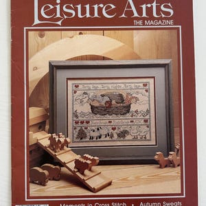 May include: A vintage issue of Leisure Arts magazine, featuring a cross stitch pattern of a boat with the text "Shorty days, Shorty nights, Shorty days". The magazine cover also features a wooden toy set with a ramp and animals.