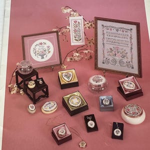 Op de afbeelding: Een verzameling kruissteekstalen en decoratieve dozen. De afbeelding toont ingelijste bloemmotieven, kleine sieradendoosjes en een hangerketting. Het kleurenpalet omvat roze, bruine en gouden accenten. De tekst "CHOICE SAMPLER" is zichtbaar.