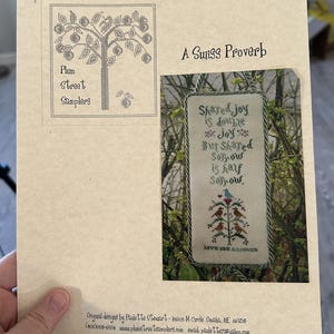 May include: A printed design for cross-stitch embroidery featuring a tree with birds and the text "Shared joy is double joy but shared sorrow is half sorrow". The design is titled "A Swiss Proverb".