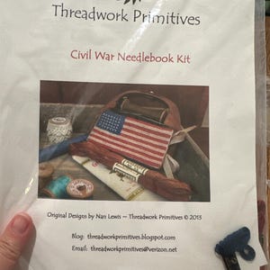 Könnte beinhalten: Ein Civil War Needlebook Kit von Threadwork Primitives. Das Set enthält ein Nadelbuch mit einem amerikanischen Flaggen-Design, Garnrollen und anderes Zubehör. Das Set ist in einer transparenten Plastiktüte verpackt.