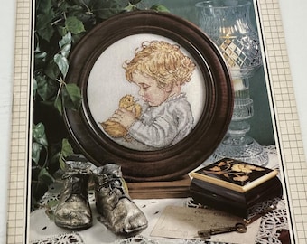 May include: A vintage issue of "Cross Stitch & Country Crafts" magazine. The cover features a framed cross-stitch of a child with a chick, antique boots, a decorative box, and a key. The magazine's title and issue details are visible.