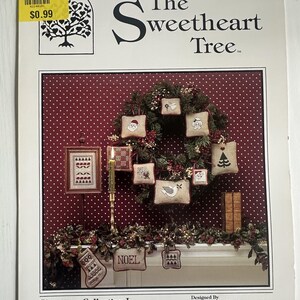 May include: A book cover titled "The Sweetheart Tree" featuring a Christmas wreath with embroidered ornaments. The cover includes the text "Christmas Collection I" and a price tag.