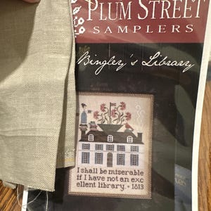 Może przedstawiać: Wzór do haftu krzyżykowego od Plum Street Samplers, zatytułowany "Bingley's Library". Projekt przedstawia szczegółową ilustrację budynku z cytatem: "I shall be miserable if I have not an excellent library. 1813." Widoczny jest kawałek jasno-beżowej tkaniny.
