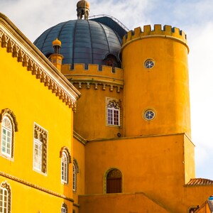 May include: A yellow building with a blue domed roof and multiple windows. The building has a tower with a round window and a pointed roof.