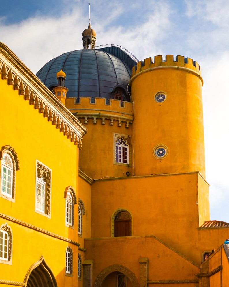 May include: A yellow building with a blue domed roof and multiple windows. The building has a tower with a round window and a pointed roof.