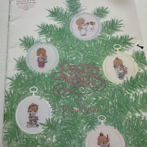 May include: A cross-stitch pattern book titled "Precious Moments in Miniature" featuring designs of Precious Moments characters in Christmas ornaments. The cover shows the ornaments on a green Christmas tree background.