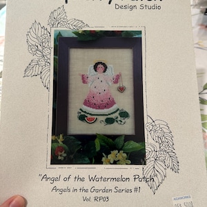 May include: A cross-stitch pattern titled "Angel of the Watermelon Patch" from Raspberry Patch Design Studio. The image features a framed cross-stitch angel in a watermelon-themed dress. The pattern is part of the Angels in the Garden Series #1.