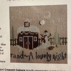 Puede incluir: Patrón de punto de cruz que representa una escena invernal con un edificio cubierto de nieve, árboles y un muñeco de nieve. El texto "rand~A lovely night" está bordado debajo del edificio. Parte de la serie "Christmasland".