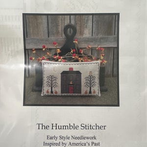 Pode incluir: Um padrão de ponto cruz intitulado "Halloween Homestead" com uma casa preta com porta vermelha, árvores e abóboras. O bordado de The Humble Stitcher é inspirado no passado americano.