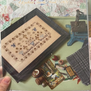 Puede incluir: Un kit de punto de cruz titulado "Bluebird of Happiness" de Elizabeth Smith, 1821. El kit incluye un sampler enmarcado con pájaros azules y motivos florales, y otros artículos relacionados con la costura. También se ve el texto "1897 Schoolhouse Samplers".
