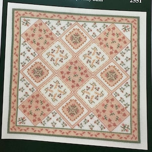 May include: A cross-stitch pattern titled "Autumn Time Quilt" designed by Cathy Bussi. The design features a repeating pattern of diamonds and squares in shades of peach, cream, and green. The text "Imaginating" and the number "2551" are also visible.