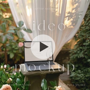 May include: A black laptop computer with a blank screen displaying a play button icon. The laptop is sitting on a stone pedestal with greenery and flowers in the background.