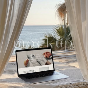 May include: A laptop computer open to a website with the text "Brand Identity & Coaching for Designers and Creatives" and "HELLO, I AM BONNIE - PERSON DEDICATED TO" on a white blanket with a view of the ocean in the background.