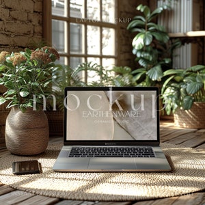 May include: A silver laptop computer with a blank screen displaying the text "Mockup Earthenware Ceramics Studio" is open on a woven straw mat. The laptop is on a wooden table with a mobile phone and a vase of flowers in the background.